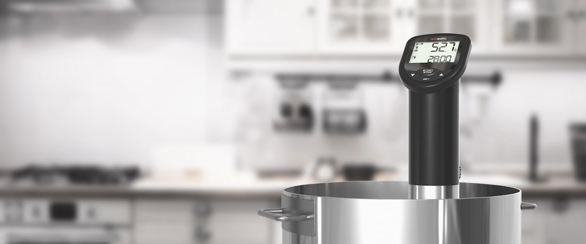 Sous-vide-Stick Sousmatic von TFA Dostmann befestigt in einem Edelstahlkochtopf. Veranschaulicht, wie einfach der Sous-Vide-Stick zu befestigen ist. Der Hintergrund zeigt eine Küche. 